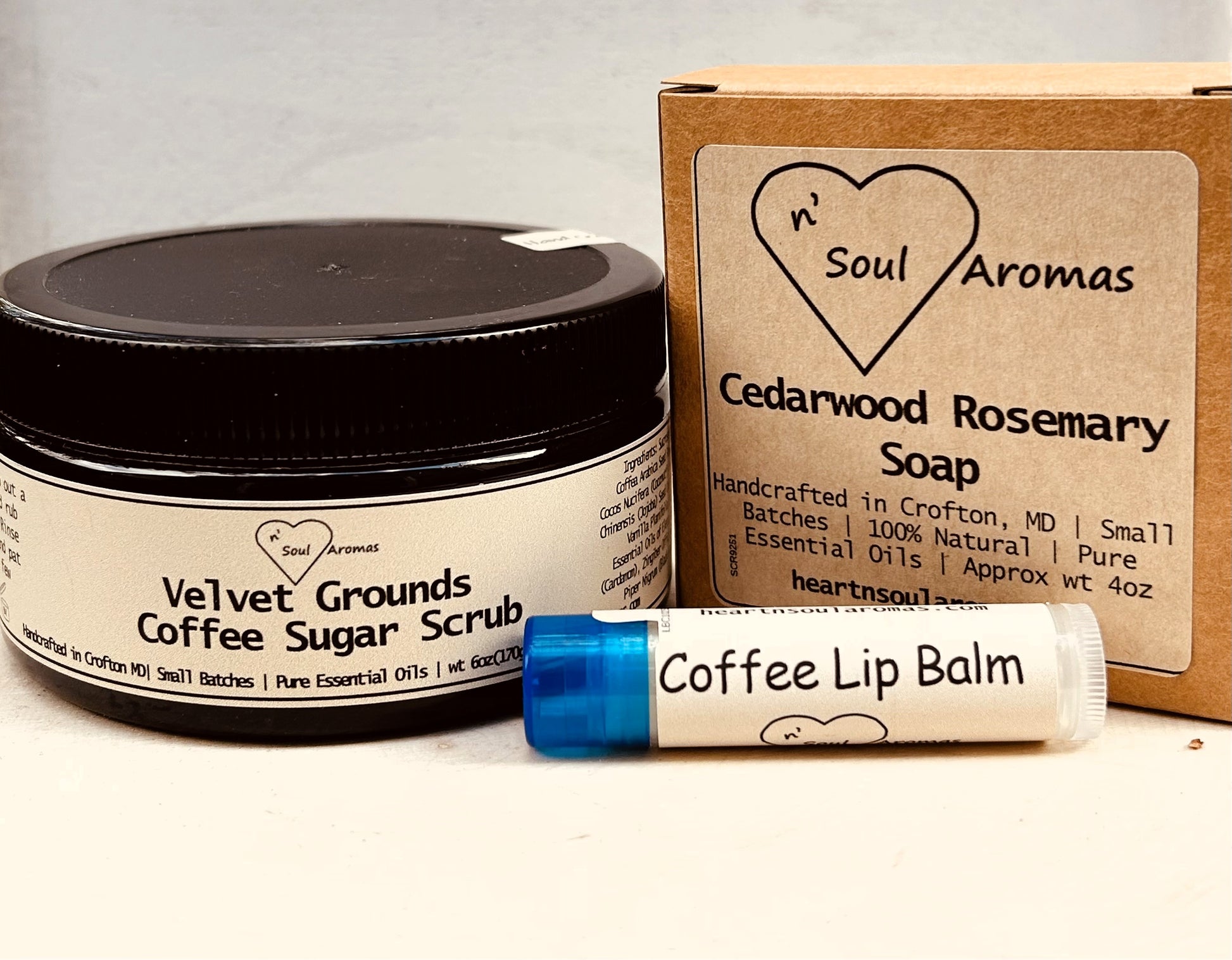 Collection of Heart 'n Soul Aromas products including coffee sugar scrub, soap, and lip balm on a neutral background.